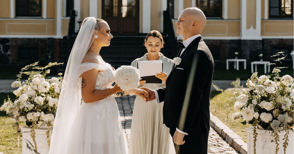 Humanistinė vestuvių ceremonija lauke. Jaunieji laikosi už rankų.